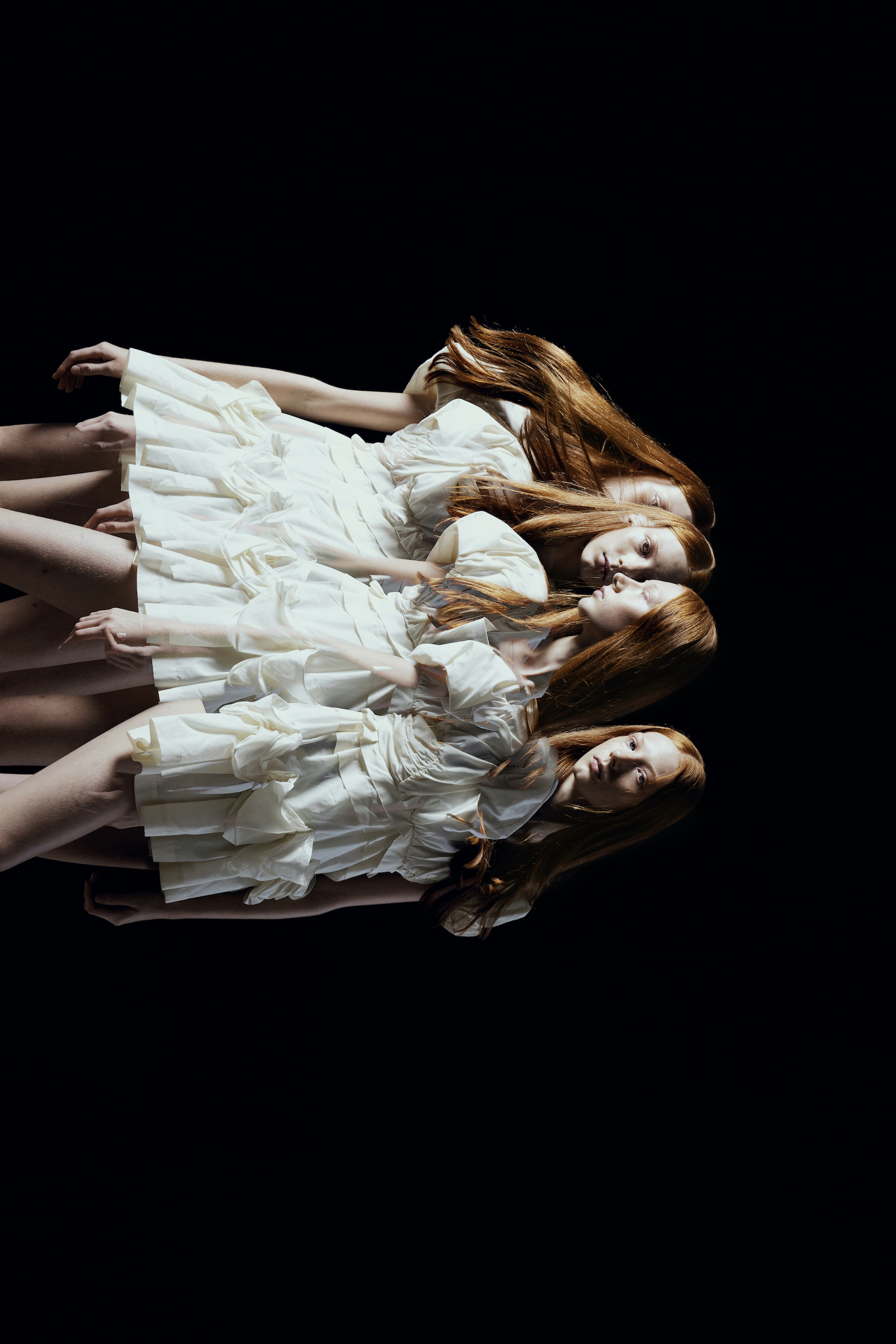 Multiple exposures of a woman with long red hair wearing a short, ruffled white dress against a stark black background in a fashion photograph.