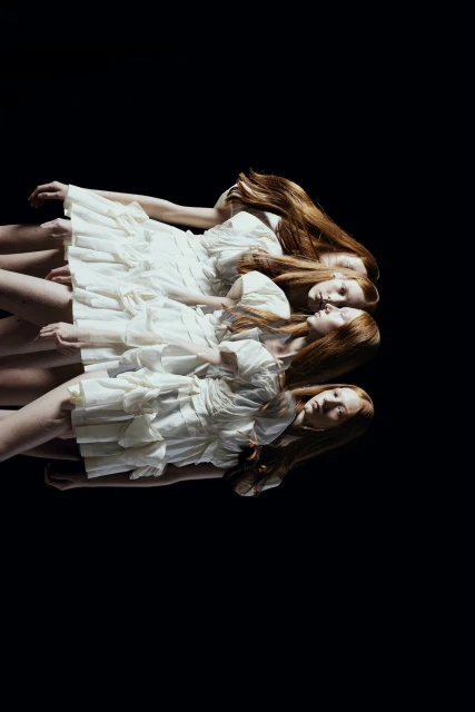 Multiple exposures of a woman with long red hair wearing a short, ruffled white dress against a stark black background in a fashion photograph.
