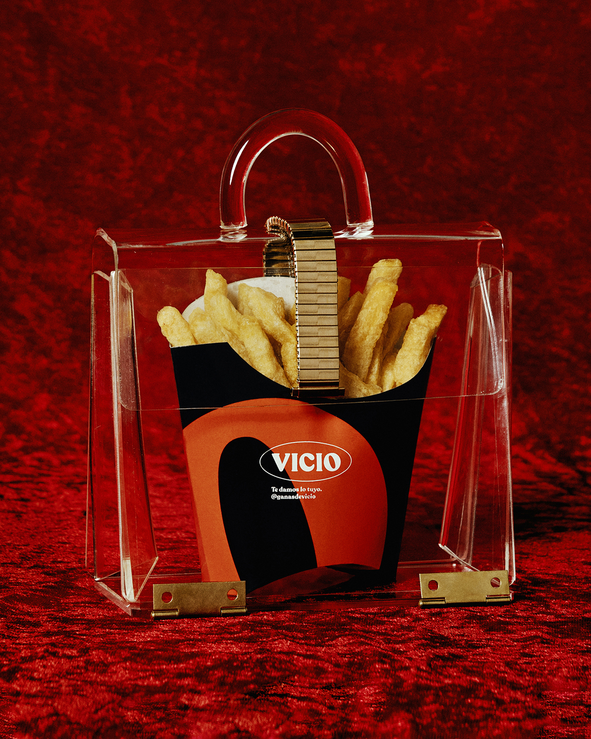 Acrylic purse containing French fries in branded container on red velvet. Minimalist studio product shot for food and fashion industries.