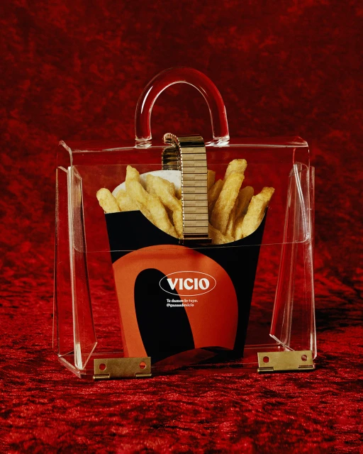 Acrylic purse containing French fries in branded container on red velvet. Minimalist studio product shot for food and fashion industries.