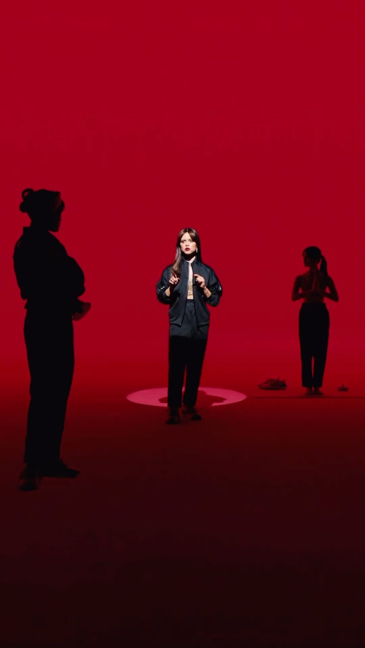 Three adult women pose in a red studio. One stands centrally, while the others are visible as silhouettes on either side.
