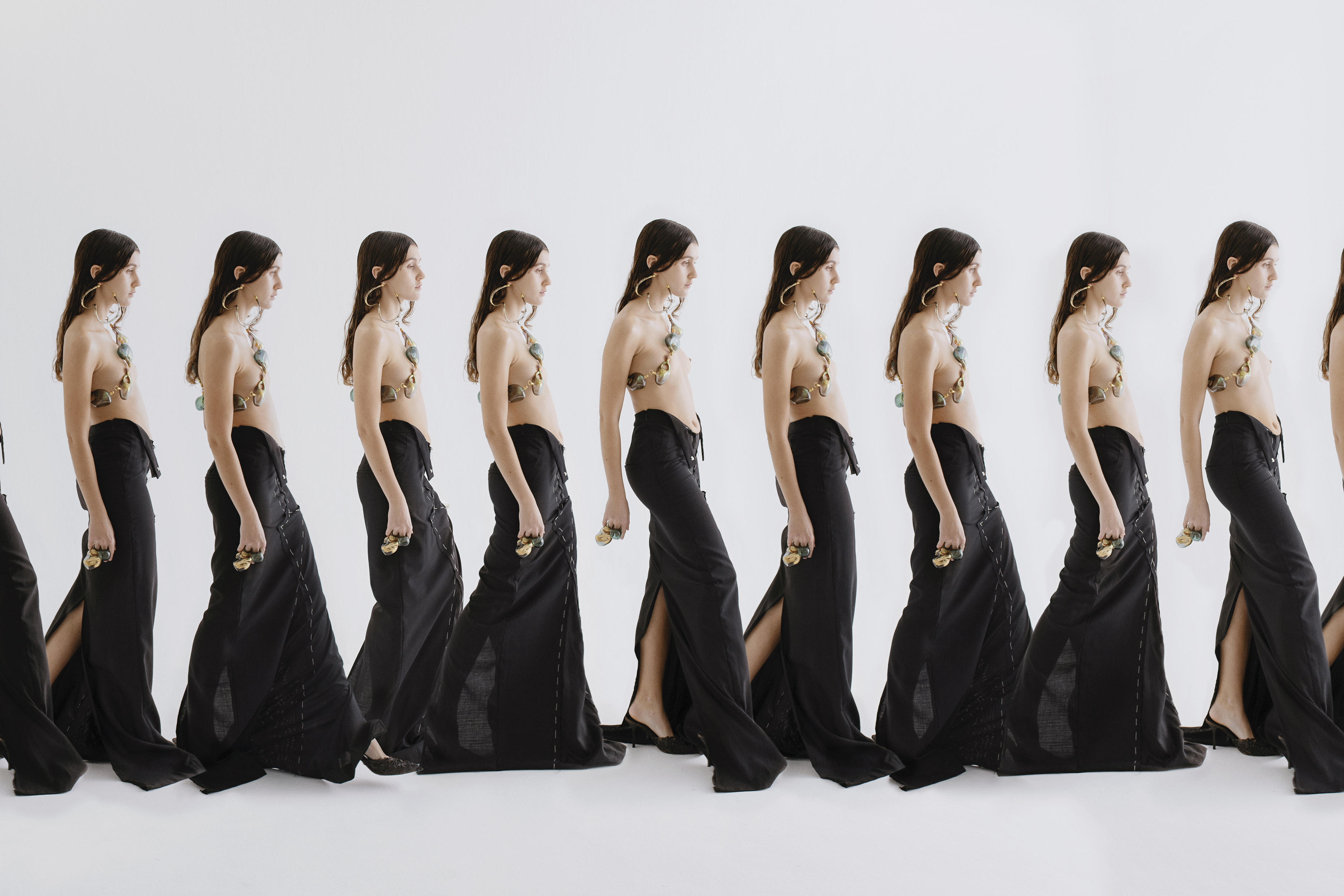 Repetitive studio image showing a fashion model wearing a halter top and a black skirt, walking against a white background.