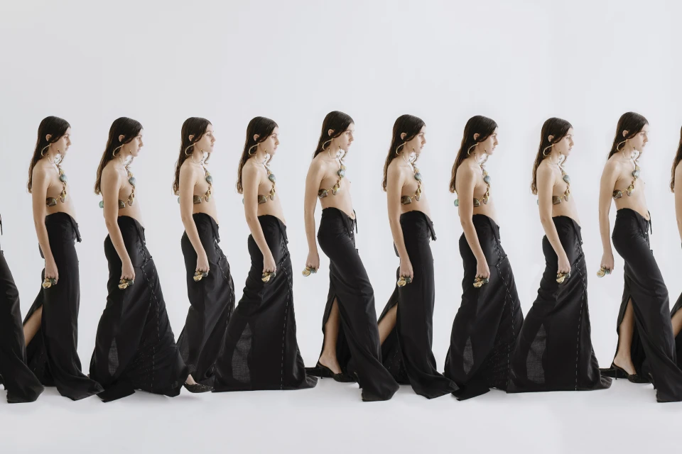 Repetitive studio image showing a fashion model wearing a halter top and a black skirt, walking against a white background.