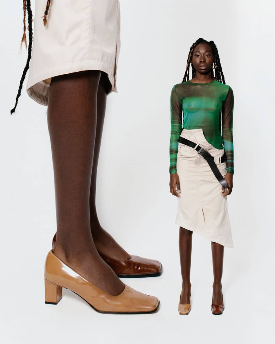 Fashion shot of two stylish African-descent women in skirts, semi-sheer tops and low block-heeled pumps, standing against a white backdrop.