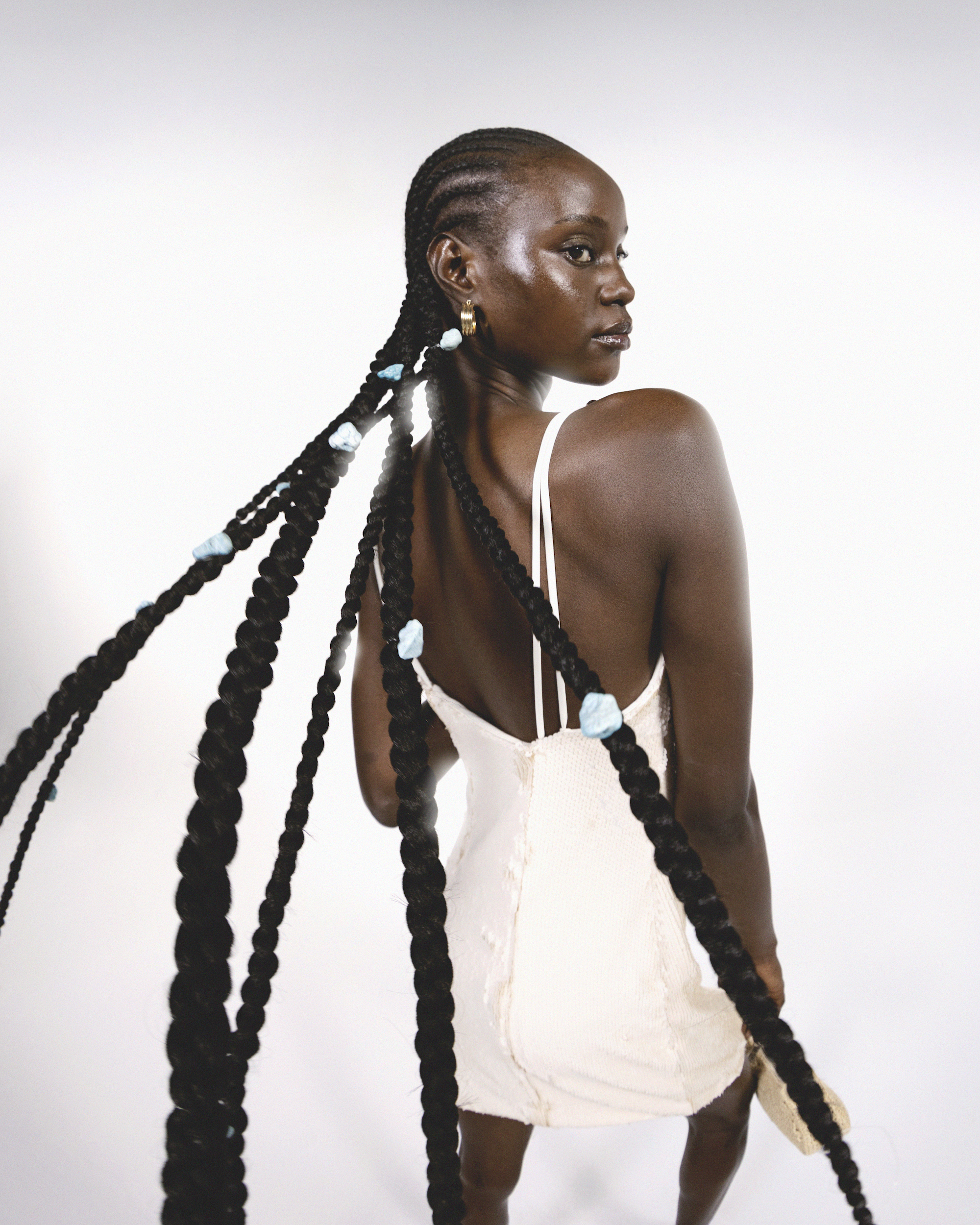 Portrait of a Black woman with braided hair, wearing a cream dress, posing in a white studio. Fashion and beauty concept.