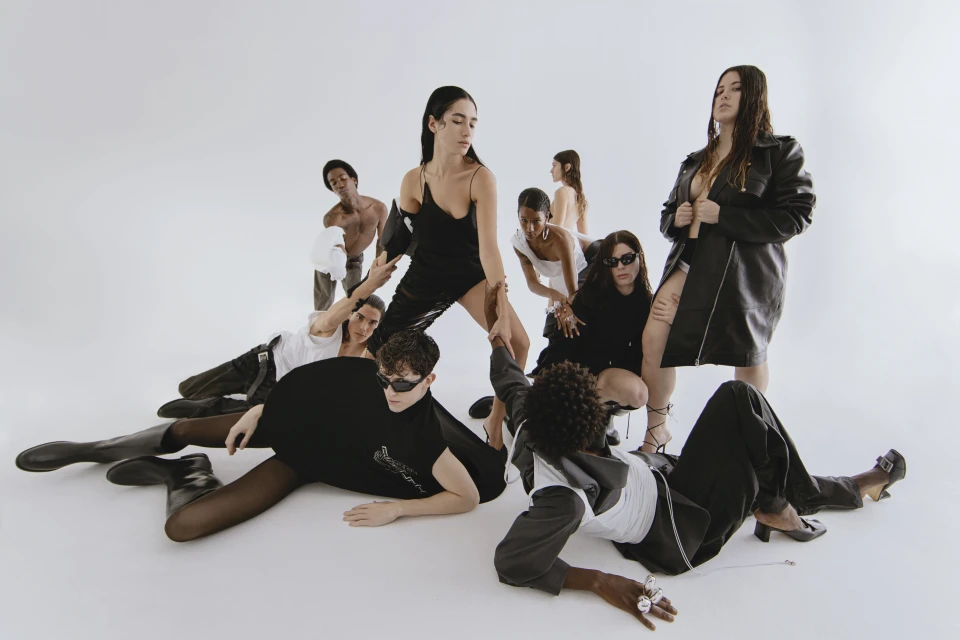 A diverse group of eight models in a white photo studio showcase avant-garde fashion, captured in a portrait-style, eye-level shot.