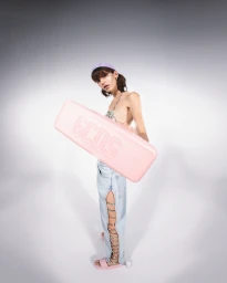 Model holding a pink GCDS case wearing light denim jeans with laced side cutouts against a grey seamless background