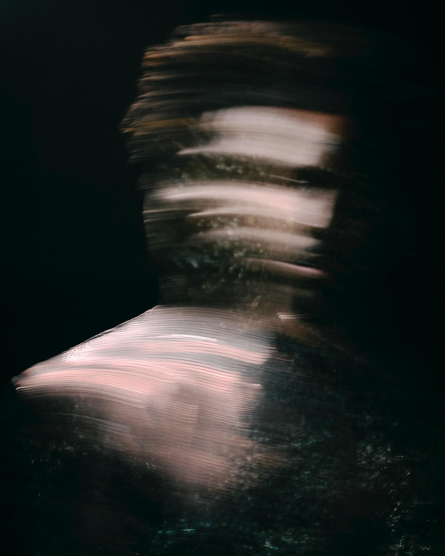 Abstract blurry portrait of a person against a dark background, creating a sense of motion and mystery, with hints of pink and brown tones.