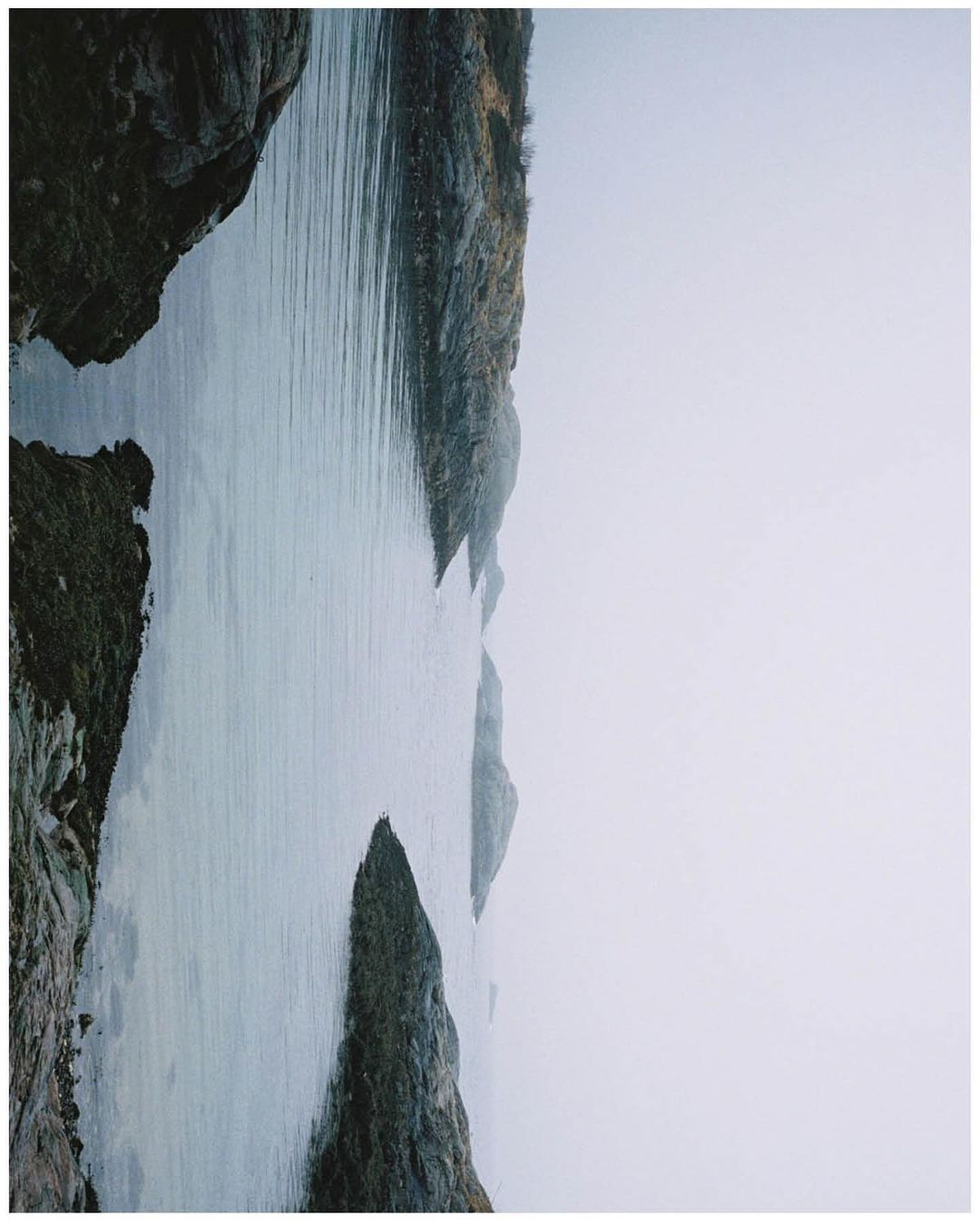 Still shot of ocean water surrounded by rocky cliffs under an overcast sky, showcasing a serene and moody seascape.