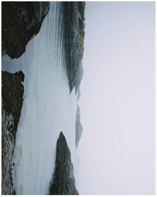 Still shot of ocean water surrounded by rocky cliffs under an overcast sky, showcasing a serene and moody seascape.