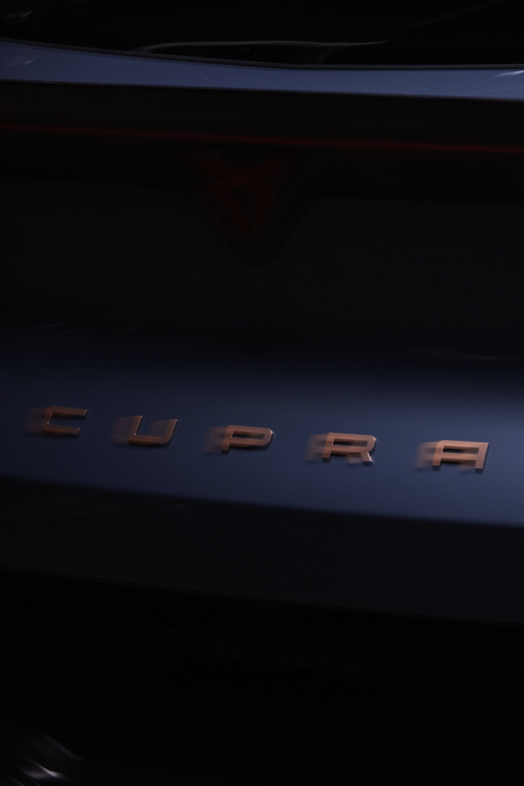 Close-up shot of a dark blue Cupra car featuring the brand name 'CUPRA' in copper lettering, creating a sleek, modern automotive image.