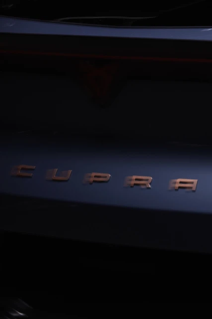 Close-up shot of a dark blue Cupra car featuring the brand name 'CUPRA' in copper lettering, creating a sleek, modern automotive image.