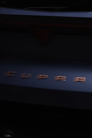 Close-up shot of a dark blue Cupra car featuring the brand name 'CUPRA' in copper lettering, creating a sleek, modern automotive image.