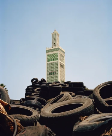 Minaret rises behind a tire pile under a clear sky. Architecture merges with the unexpected, creating a striking juxtaposition.