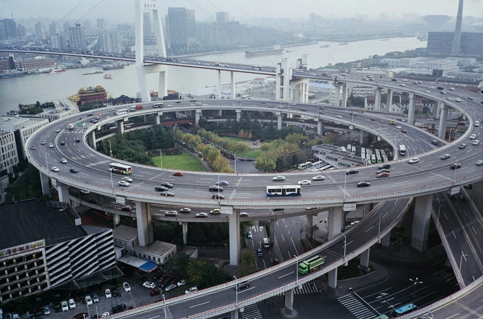 Elevated highway with multiple tiers shows cars and buses moving through a city, with bridges and buildings in the background on a foggy day.