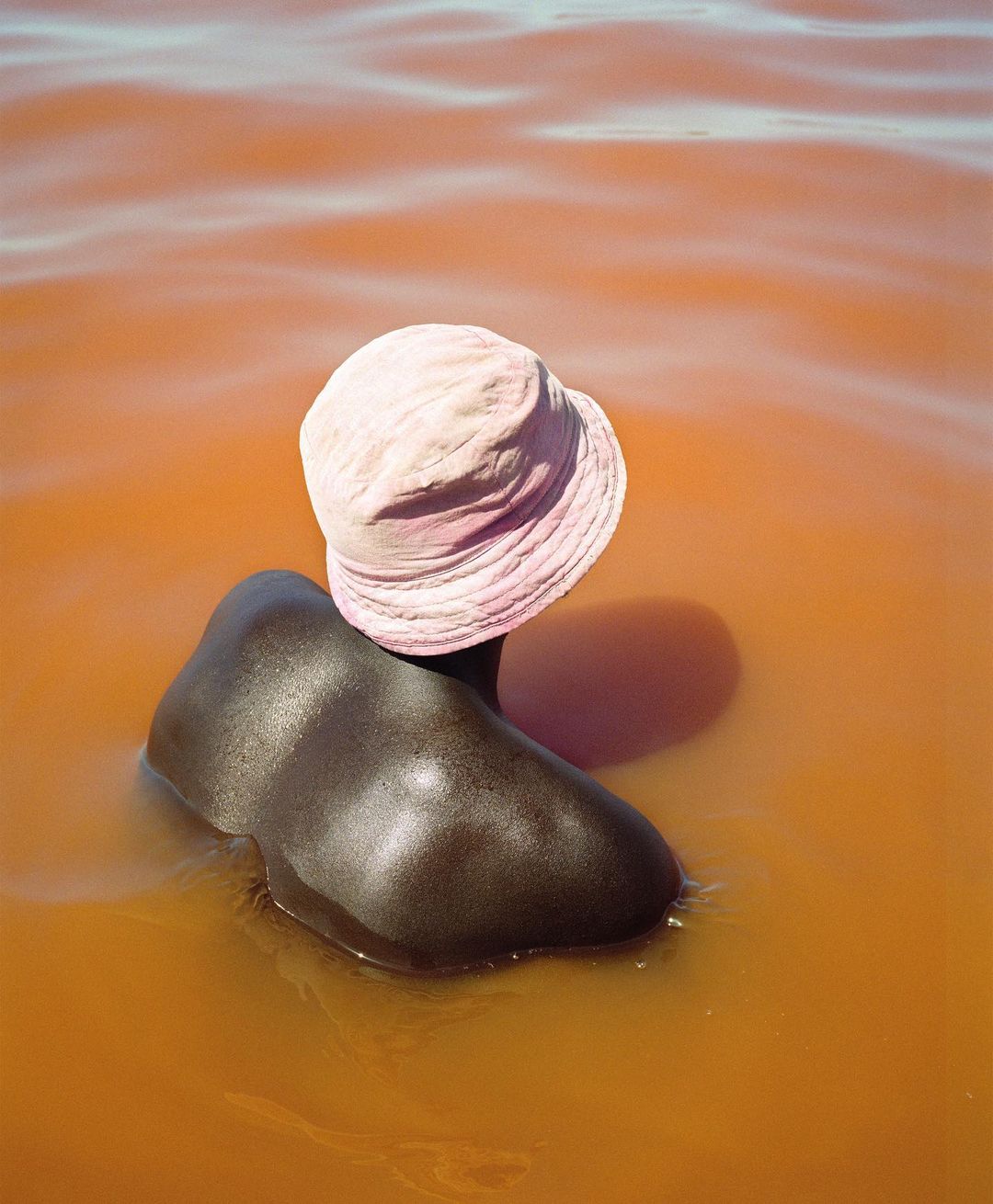 Person in water with pink hat. An African person is shown from the shoulders up, wearing a pink hat and surrounded by water.