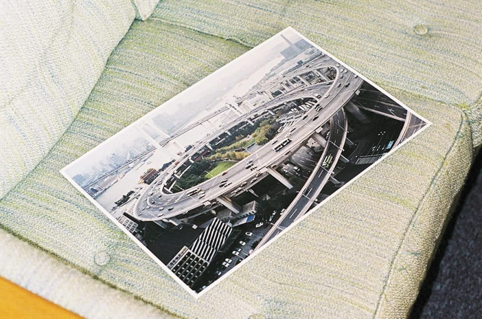 Elevated view photograph of a highway interchange in an urban area with buildings, trees, and a river, resting on a light-green couch.
