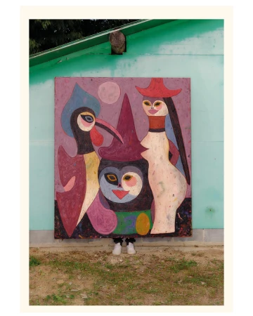 A person hidden behind a large painted artwork featuring stylized figures mounted on a teal wall outdoors