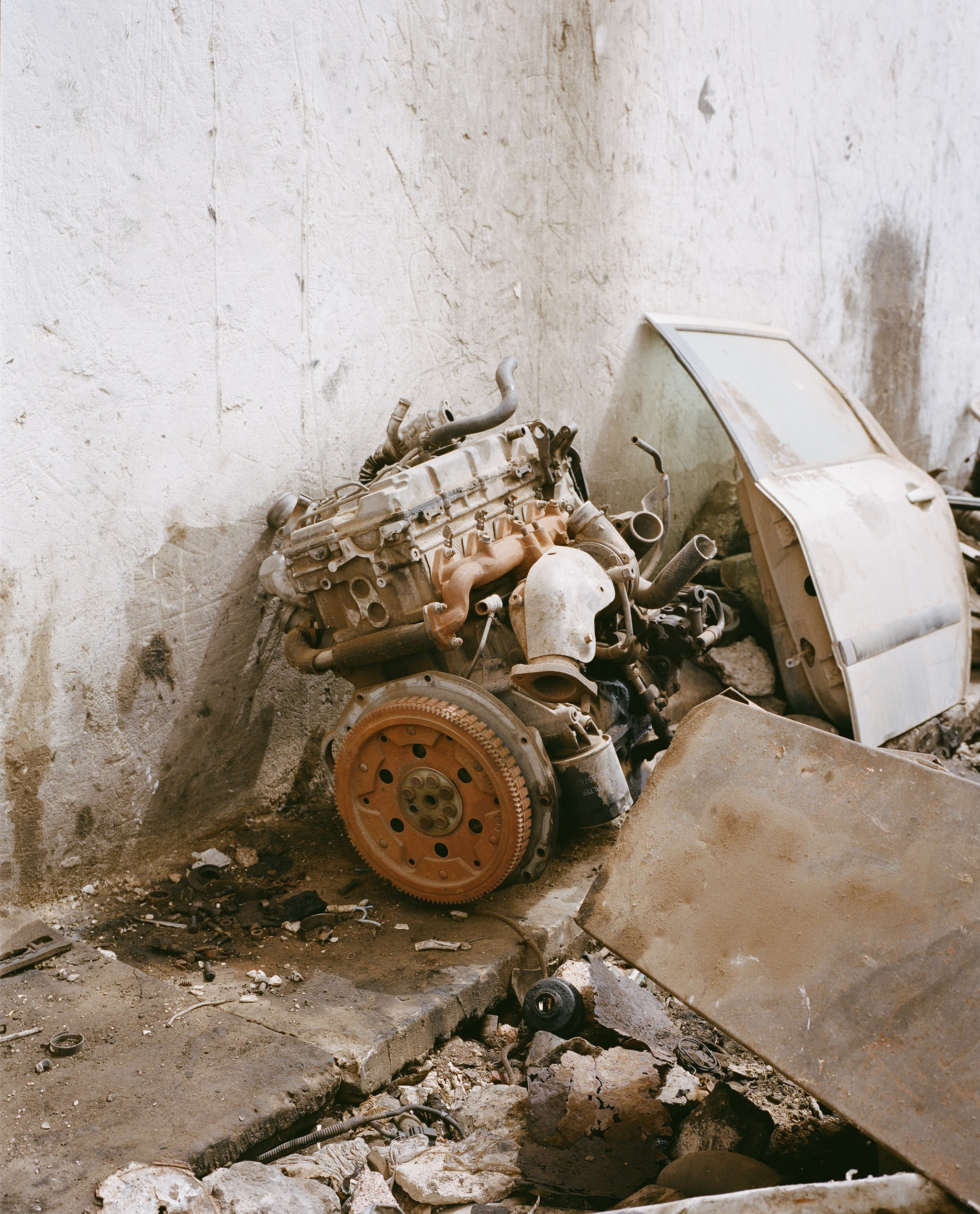 Dirty car engine and door discarded in an old room. Rust-colored engine sits near a white car door with chipped paint and debris.
