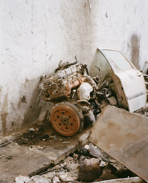 Dirty car engine and door discarded in an old room. Rust-colored engine sits near a white car door with chipped paint and debris.
