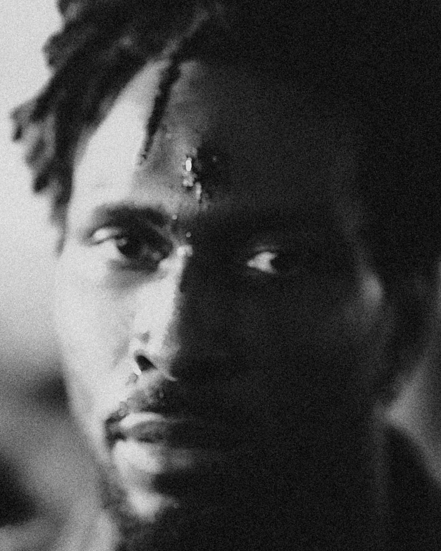 Close-up monochrome portrait of a Black man with textured hair and a serious expression captured in heavy film grain