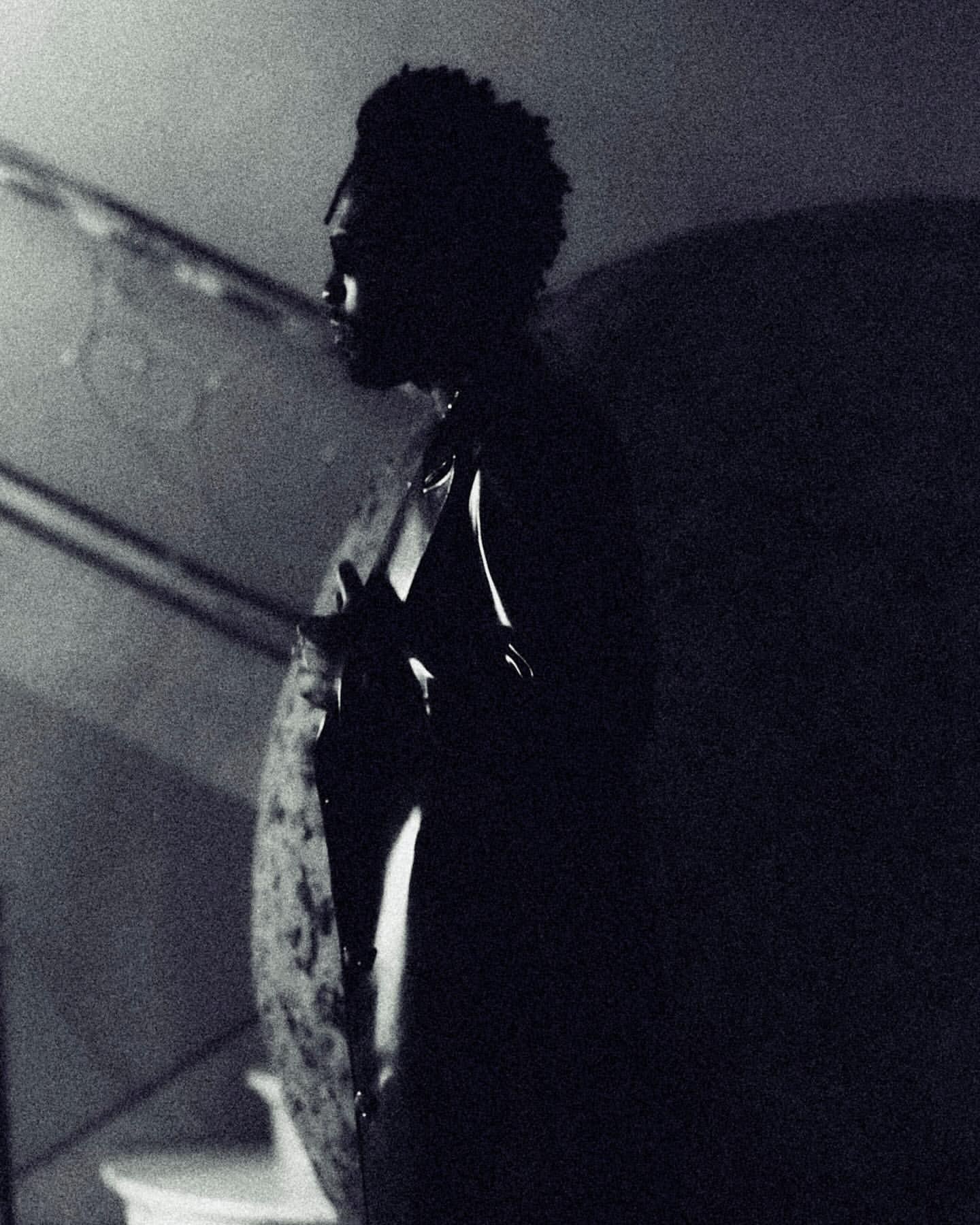 Monochrome portrait of a man in profile, depicted in a low-key lighting scheme against a shadowy interior backdrop.
