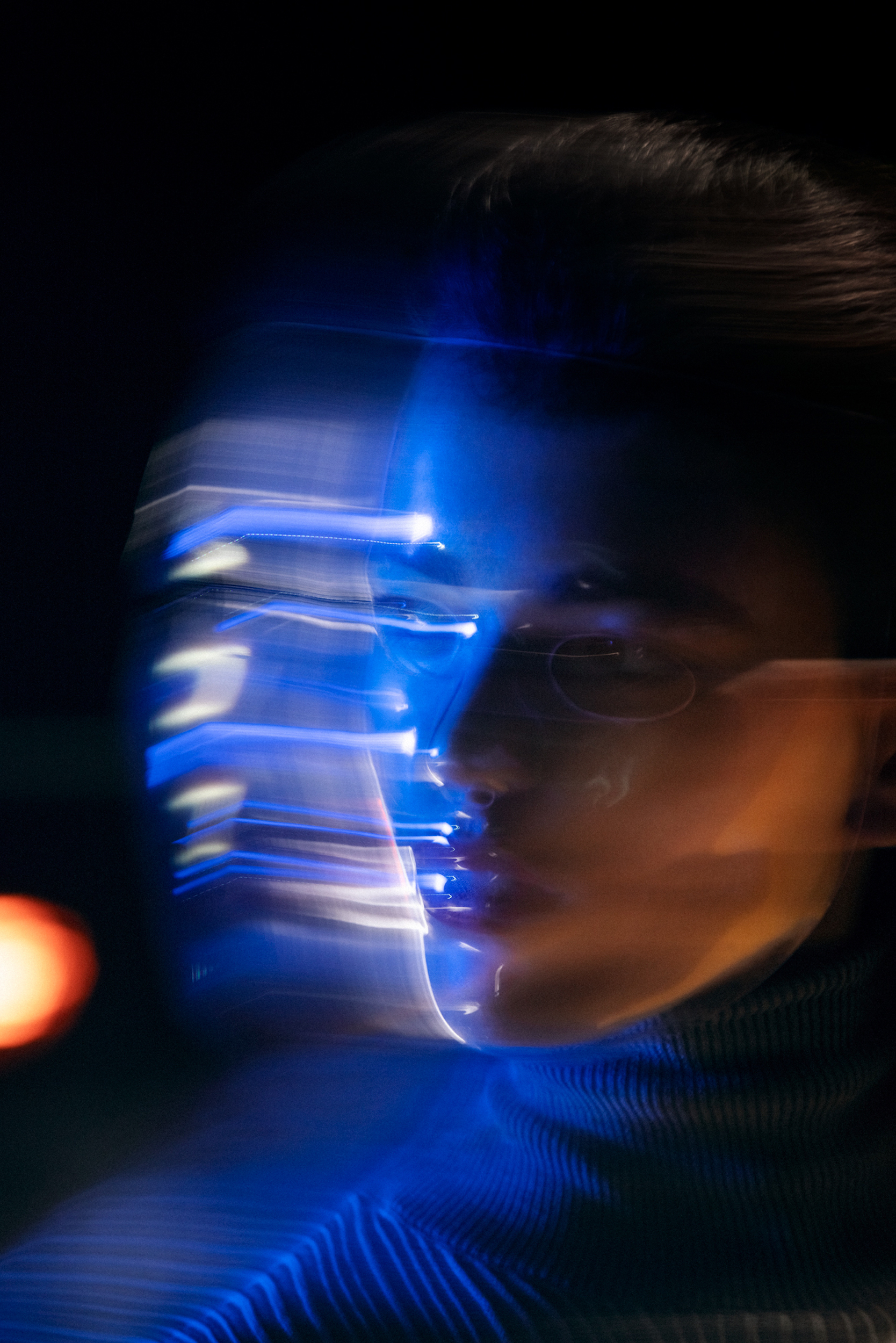 Abstract portrait of a person with blurred motion and blue lighting effects against a dark backdrop, showcasing creative photography techniques.