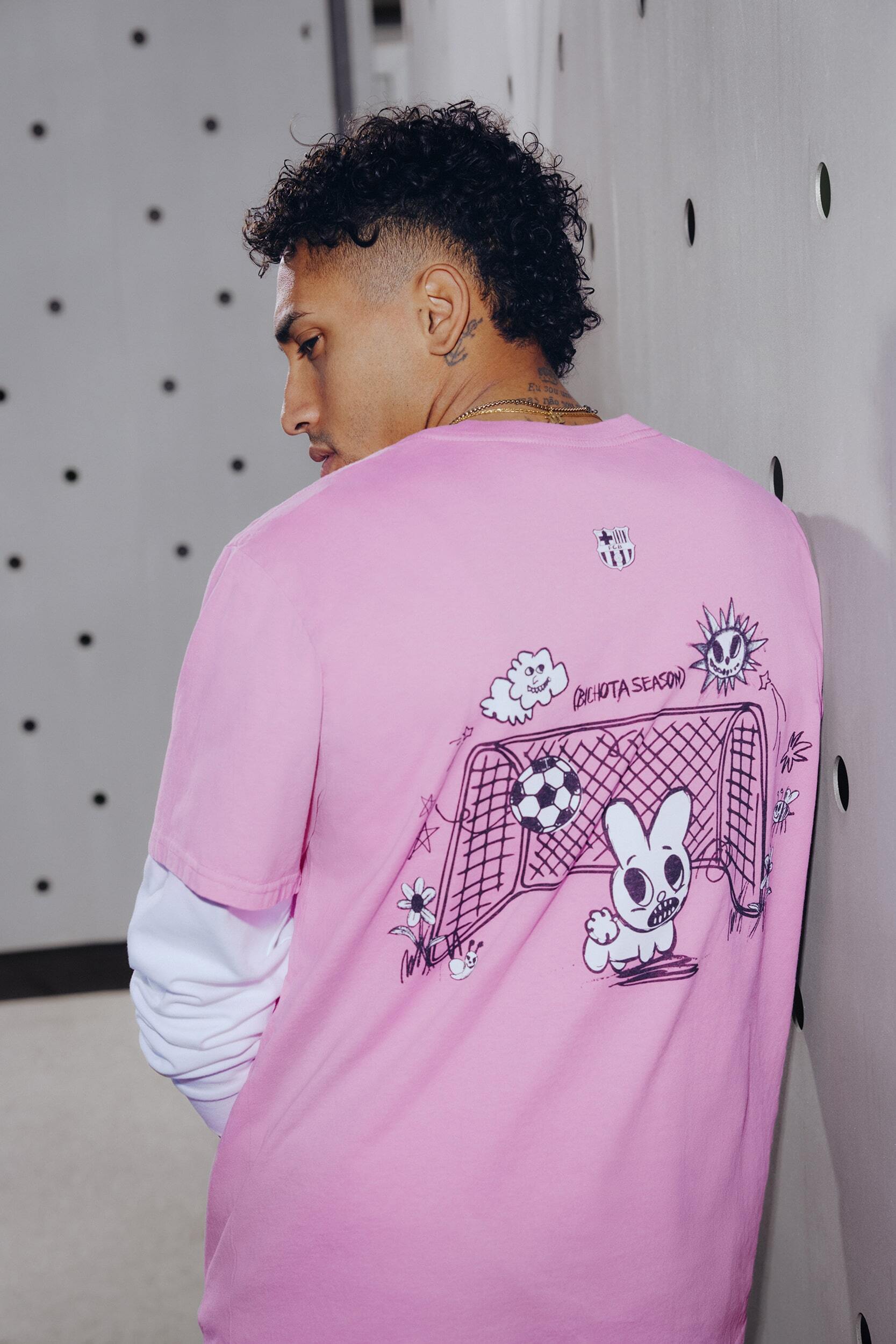 Adult male wearing a pink t-shirt with cartoon graphics standing in a room with light grey and black dot patterned wall.