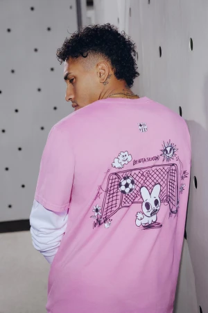 Adult male wearing a pink t-shirt with cartoon graphics standing in a room with light grey and black dot patterned wall.