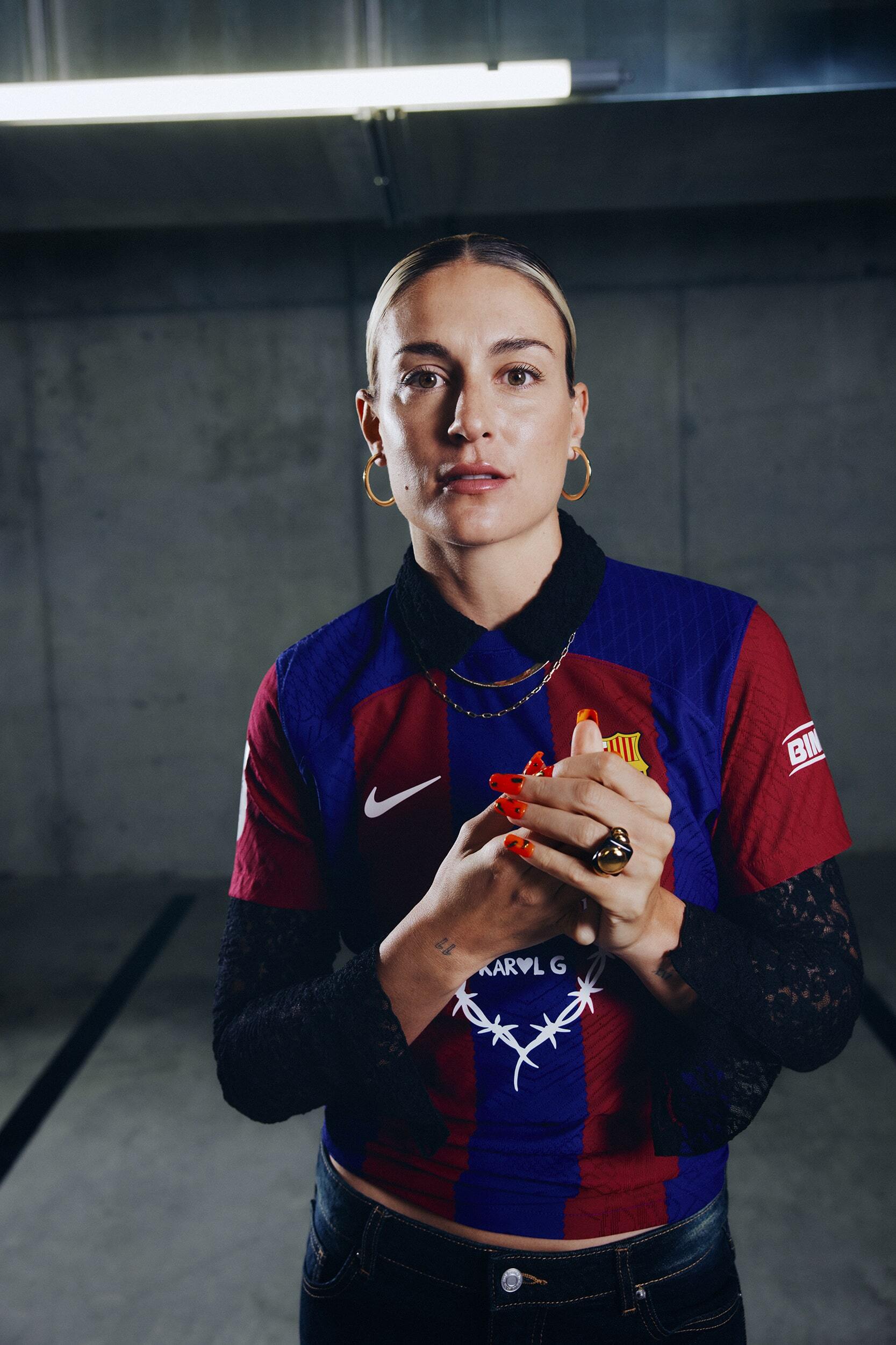 Woman in soccer jersey with red nails and gold jewelry in an indoor parking garage. Modern fashion meets sporty casual style.