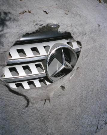 Mercedes-Benz logo and grill visible through a hole in a grey car cover. Close-up shot.