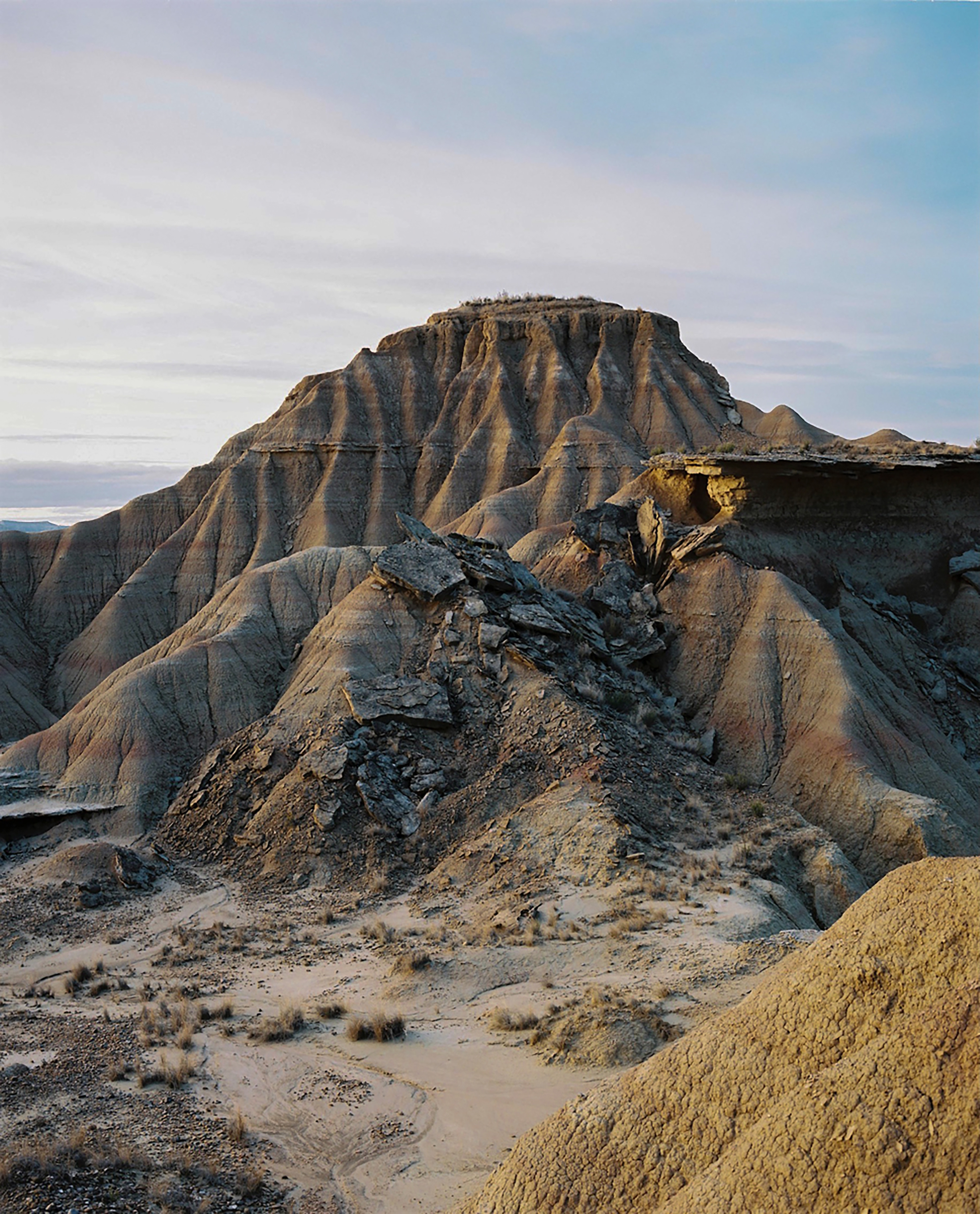 Desert landscape featuring arid rocky hills and mountains under a pale blue sky with clouds, showcasing natural terrain and geology.