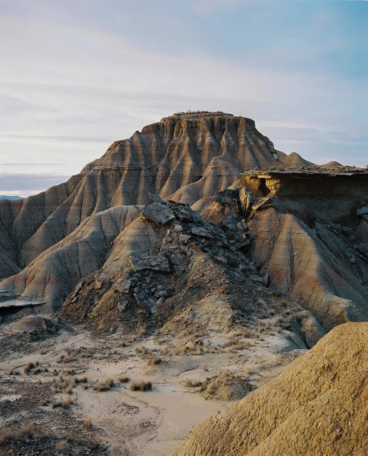 Desert landscape featuring arid rocky hills and mountains under a pale blue sky with clouds, showcasing natural terrain and geology.