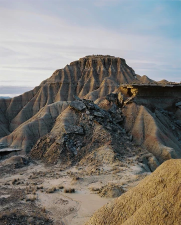 Desert landscape featuring arid rocky hills and mountains under a pale blue sky with clouds, showcasing natural terrain and geology.