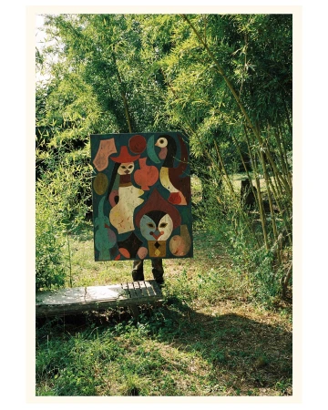 Person holding a colorful abstract painting in a green outdoor setting with bamboo, creating a juxtaposition of art and nature.