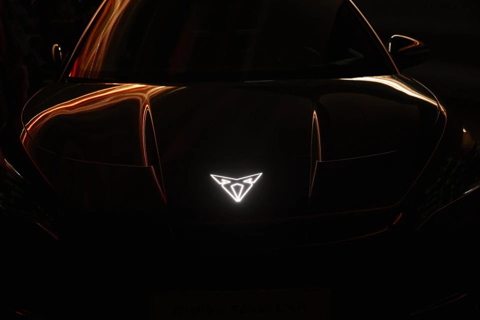 Close-up of a sleek black car featuring a glowing emblem on the hood, highlighted by light streaks in a dark environment.
