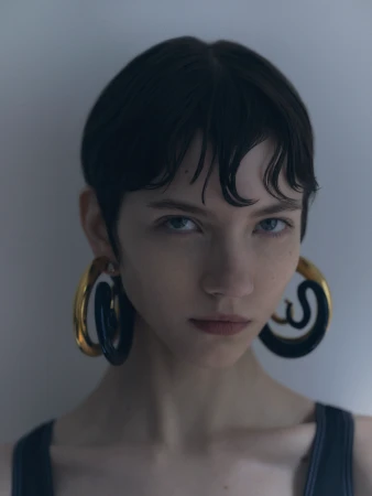 Close-up portrait of a woman with short wet-look dark hair and large sculptural gold hoop earrings by photographer Dani Pujalte.