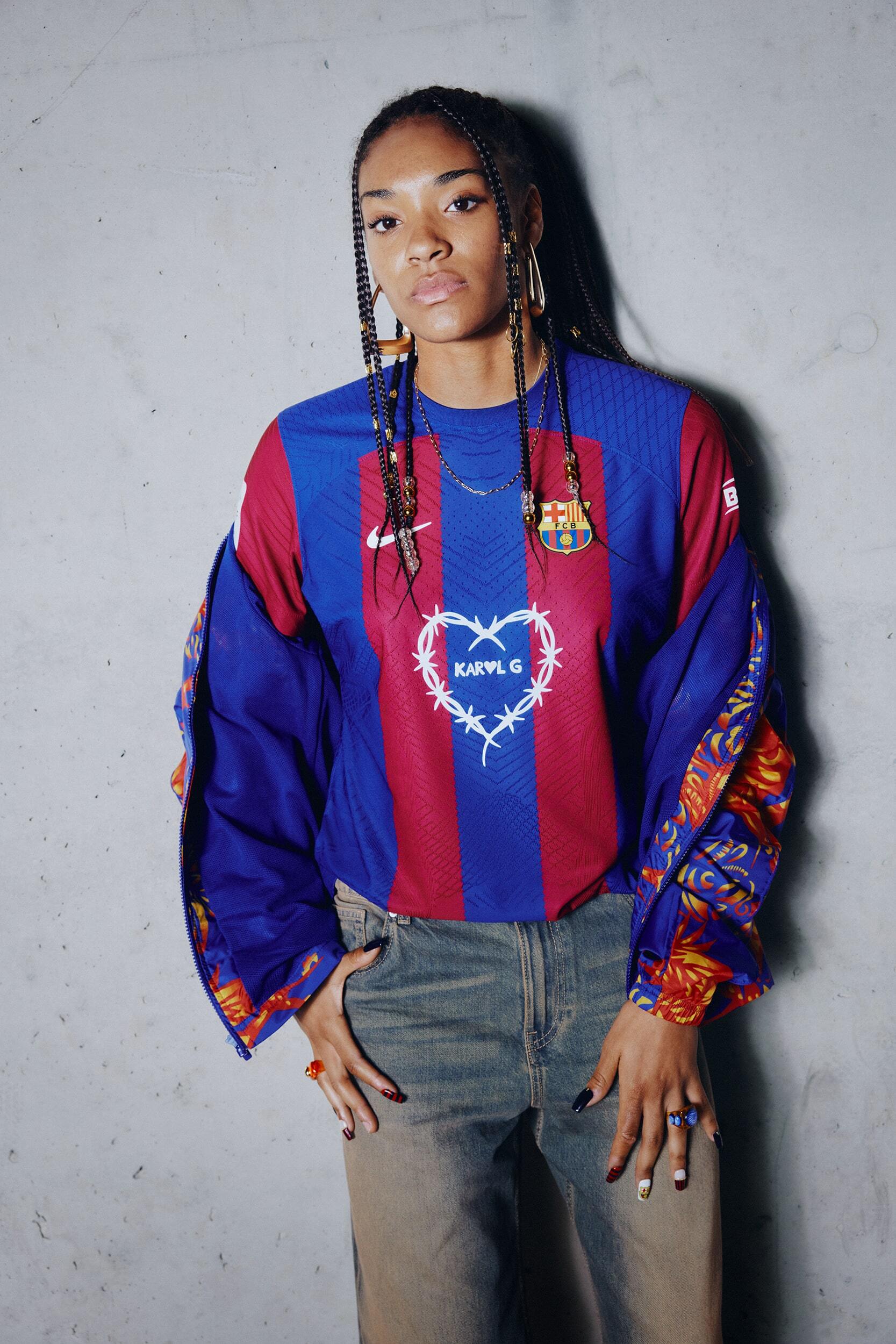 Young woman poses in a Barcelona soccer jersey and jeans in a studio setting, showcasing a casual yet fashionable look.