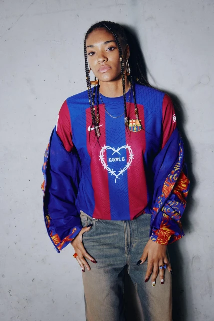 Young woman poses in a Barcelona soccer jersey and jeans in a studio setting, showcasing a casual yet fashionable look.