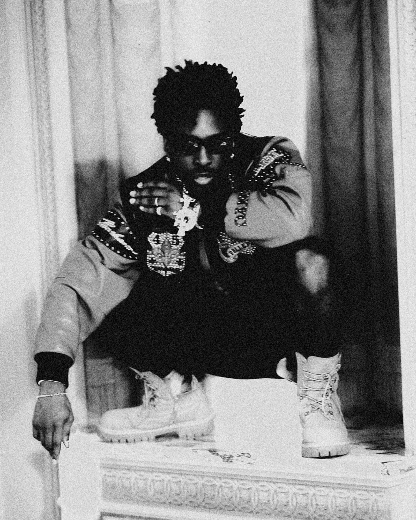 Black man crouching in patterned bomber jacket and boots photographed in black and white by Dani Pujalte