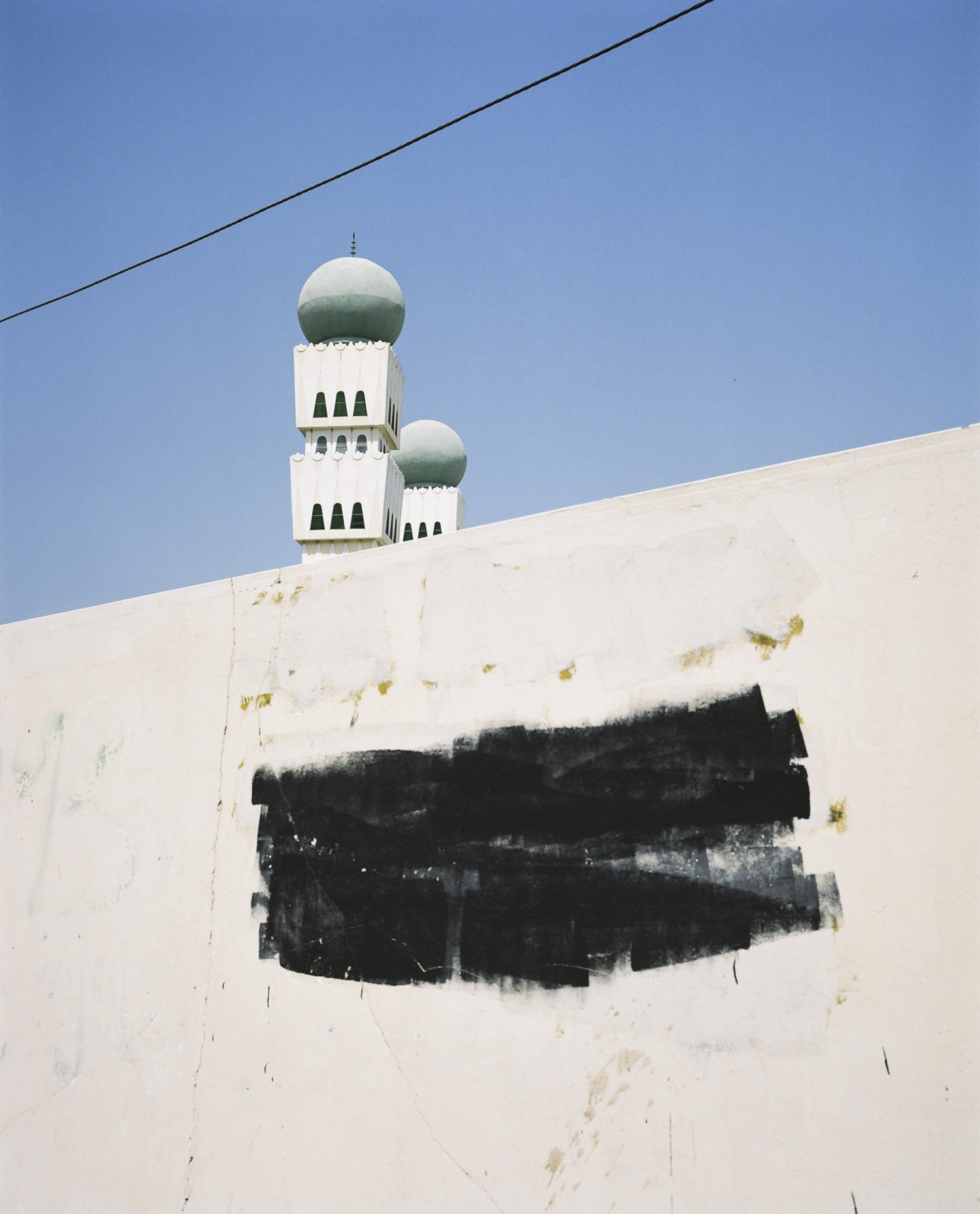 Architectural shot of a white building with distinctive green-domed towers against a clear blue sky, creating a serene architectural scene.