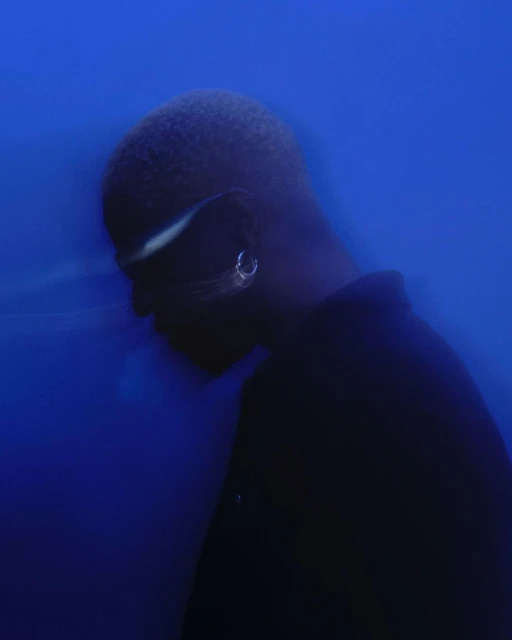 Person in profile wearing silver earrings and reflective glasses against a blurry gradient blue background in a minimalist composition.