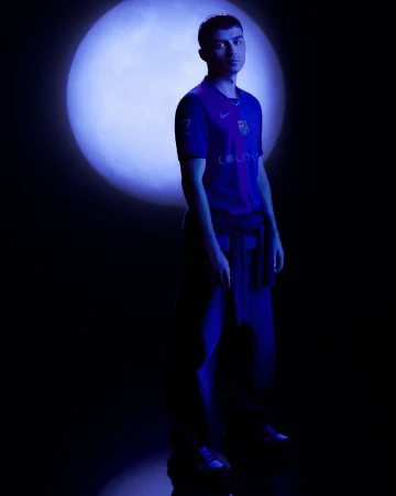 Young man in purple and blue jersey standing against a large glowing blue circular light source in a dark studio.