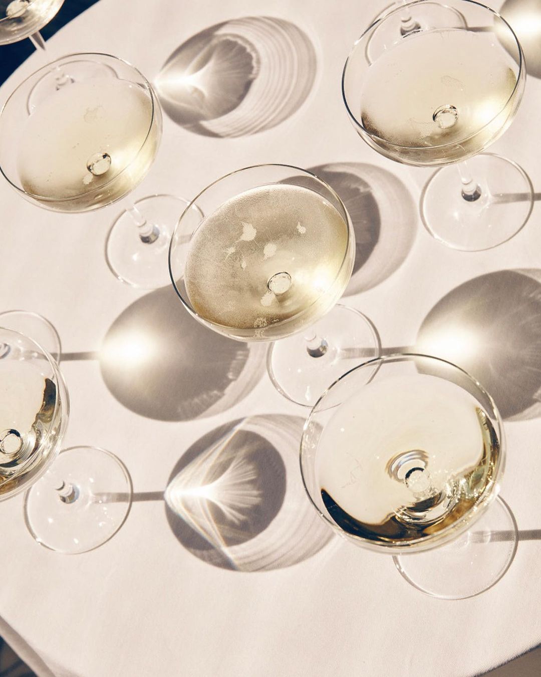 Overhead shot of champagne glasses filled with bubbly liquid, arranged on a white surface with long shadows from direct sunlight.