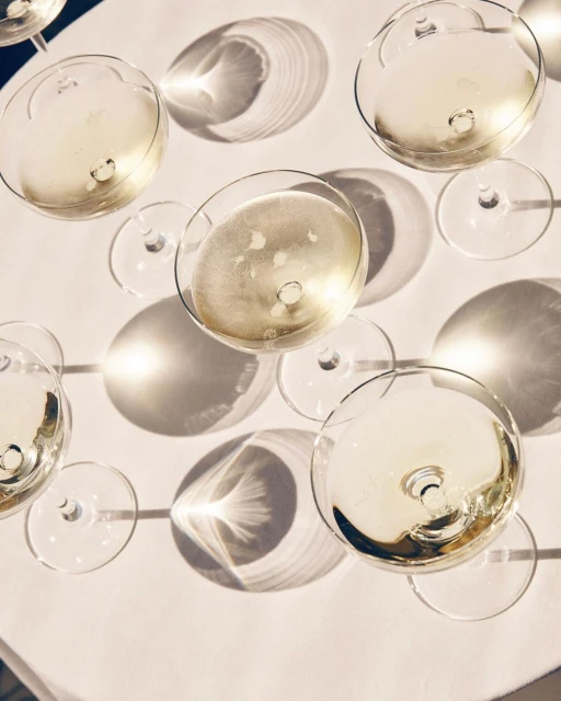 Overhead shot of champagne glasses filled with bubbly liquid, arranged on a white surface with long shadows from direct sunlight.