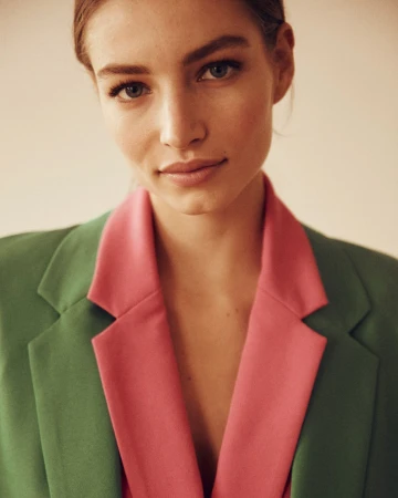 Portrait of a woman wearing a green blazer with pink lapels against a neutral background by photographer Manu Fauque.
