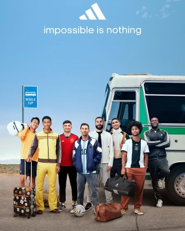 Group of soccer players stand near a bus on an open road in an Adidas advertisement, wearing soccer apparel and holding sports bags.