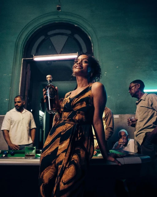Elegant woman in patterned dress holds liquor bottle, enjoying drinks at a bar with friends under moody lighting and green walls.
