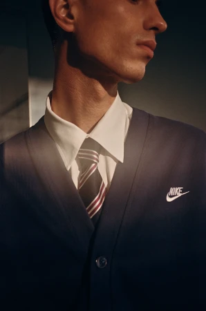Close-up portrait of a man wearing a white collared shirt, striped tie, and dark blue cardigan by photographer Manu Fauque.