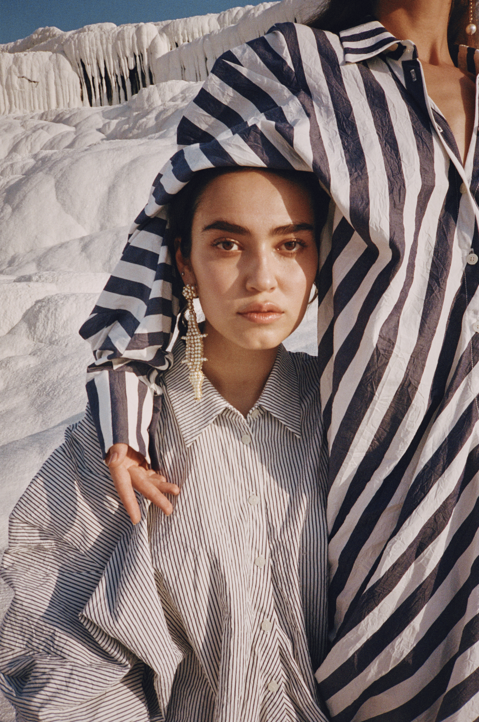 Two women in striped shirts pose outdoors near a textured white rock formation, with one woman partially covering the other with her shirt.